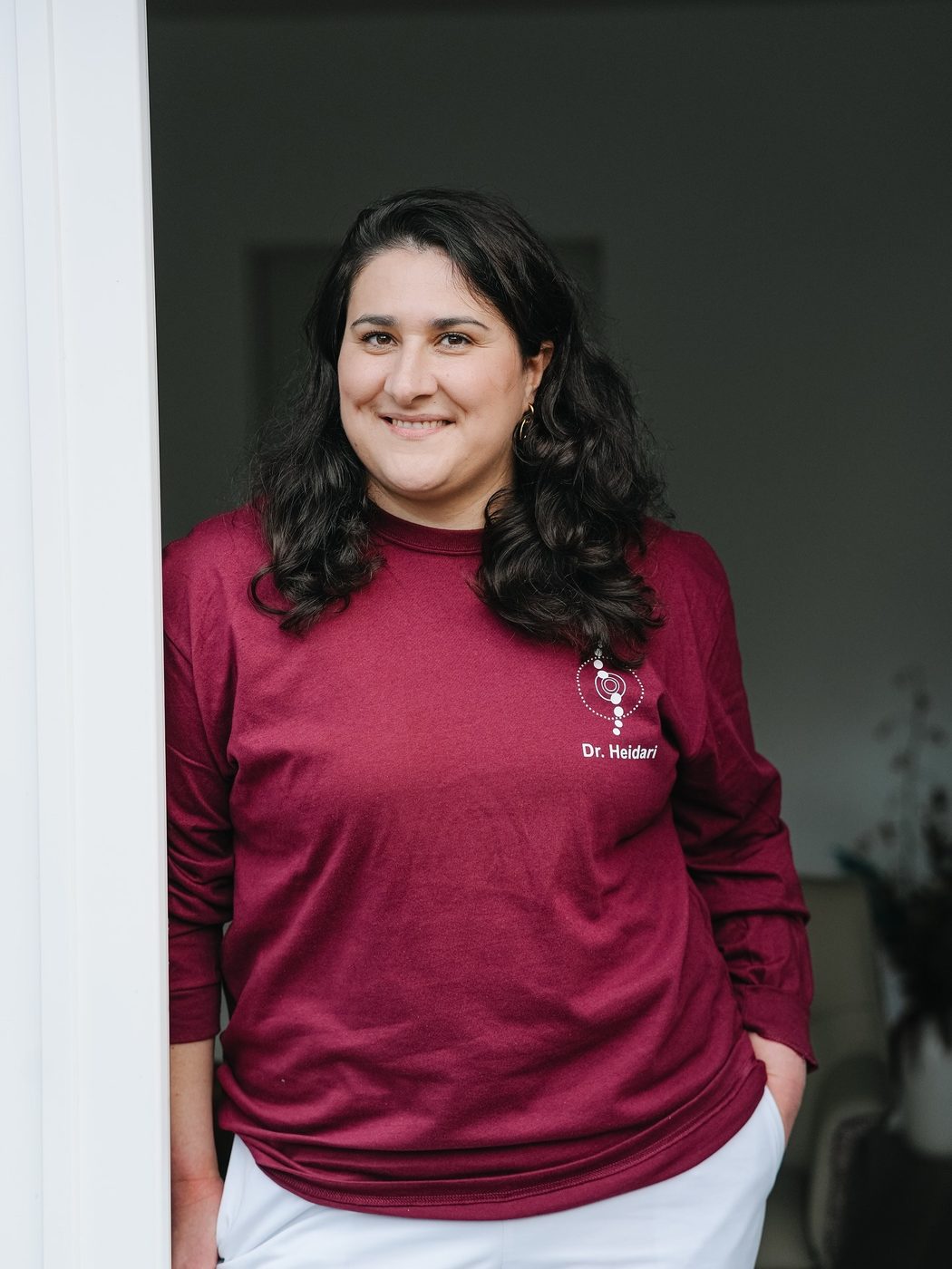 Dr. Nika Heidari im roten Praxis-Shirt, an eine Tür ihrer Praxis gelehnt