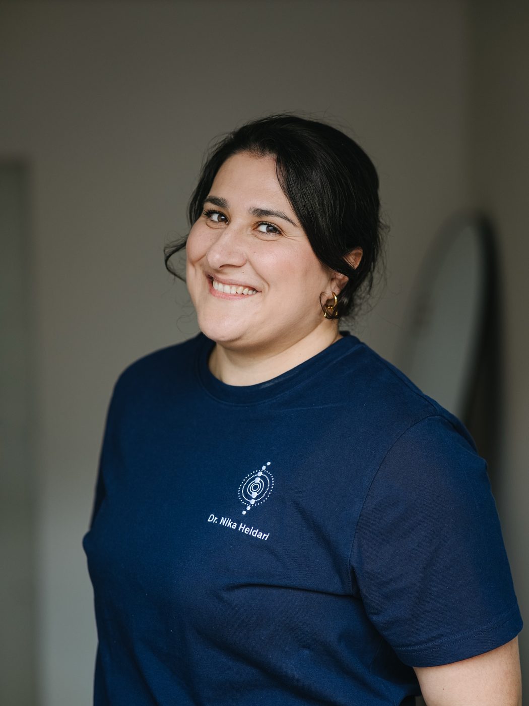 Dr. Nika Heidari lächelnd im dunkelblauen Praxis-Shirt in ihrer Praxis in Hamburg-Winterhude