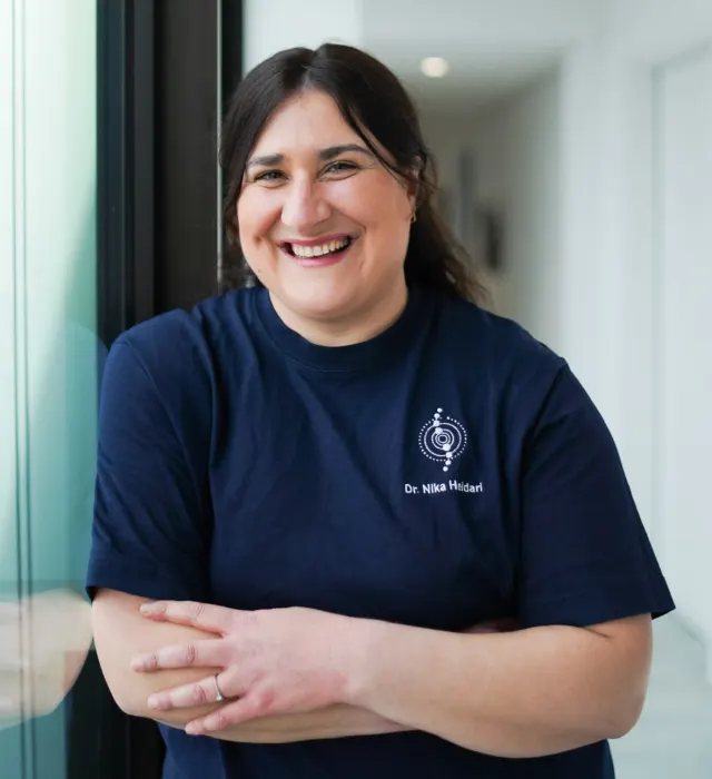 Dr. Nika Heidari lächelnd mit verschränkten Armen in ihrer Praxis